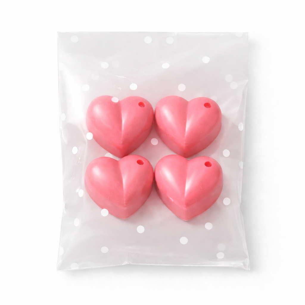 Four pink heart-shaped wax melts in a clear plastic bag with white polka dots on a white background